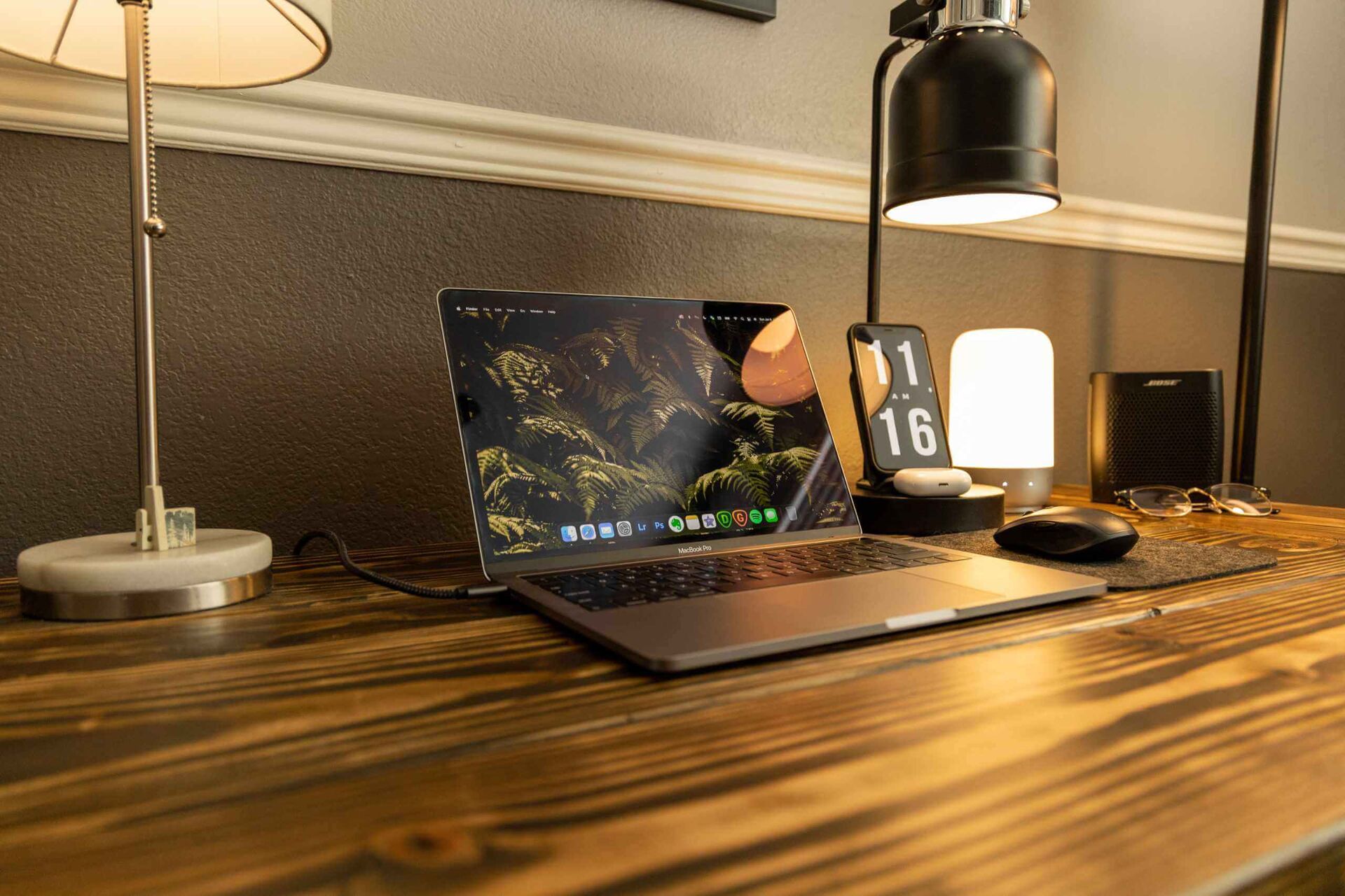 Ein Schreibtisch, auf dem ein Laptop zu sehen ist, links und rechts daneben Lampen und ein Smartphone