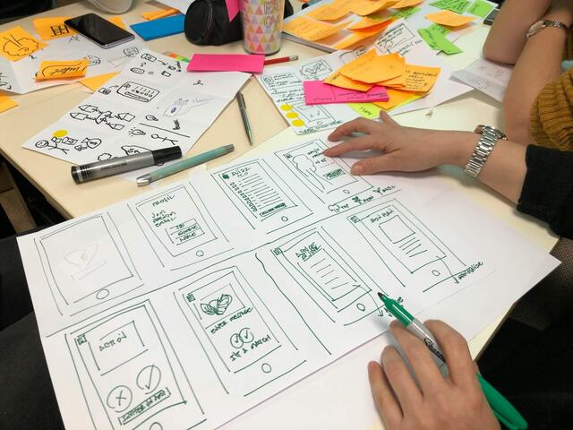 Ein Team von Personen sitzt am Tisch und entwirft Designs auf Papier