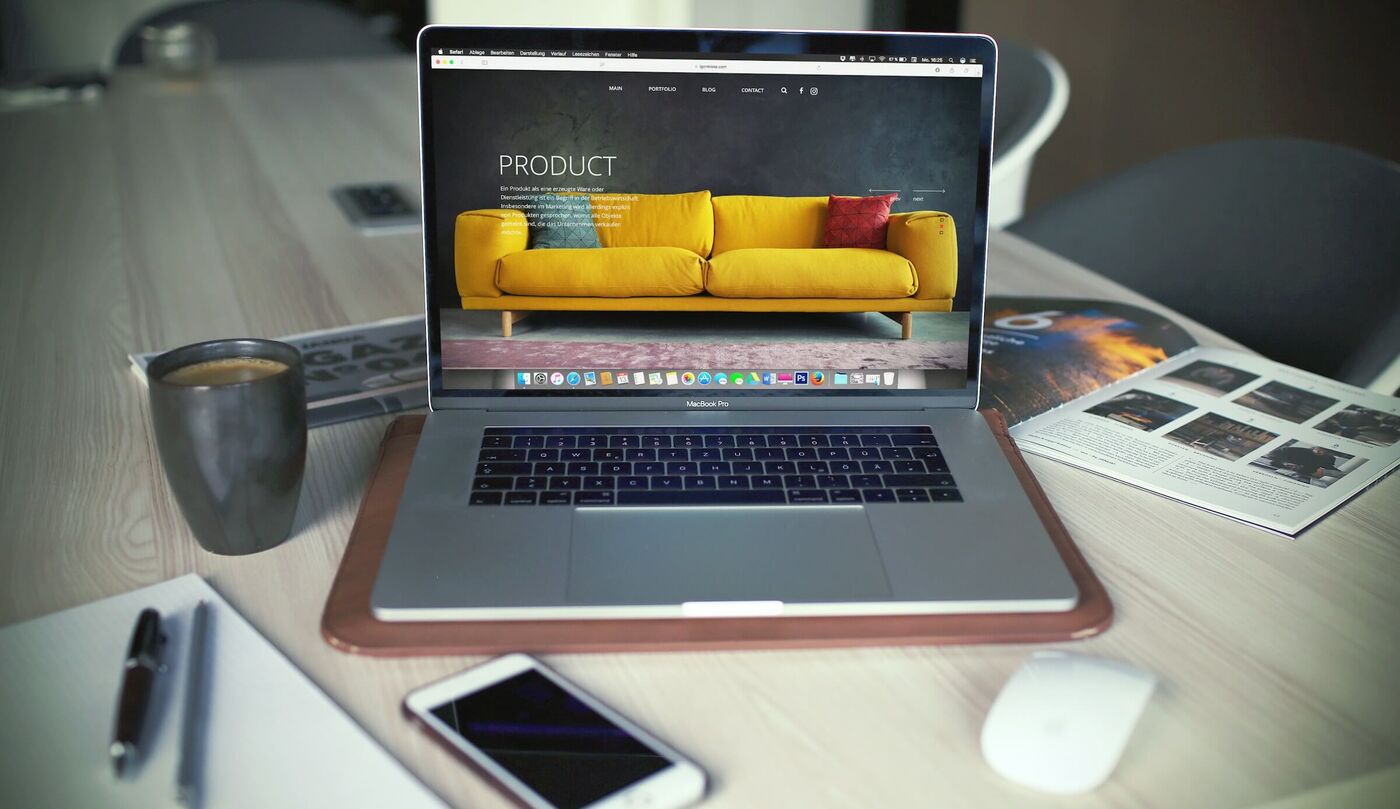 Auf einem Schreibtisch steht ein Laptop, daneben eine Tasse Kaffee und Smartphone. Auf dem Laptop ist ein Online-Shop zu sehen.